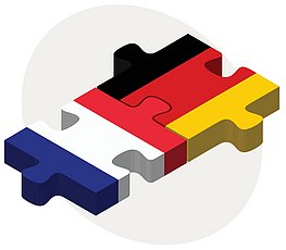 Zwei Puzzlestücke, die miteinander verbunden sind. Auf dem einen Puzzlestück ist die französische Flagge abgebildet und auf dem anderen ist die deutsche Flagge zu erkennena